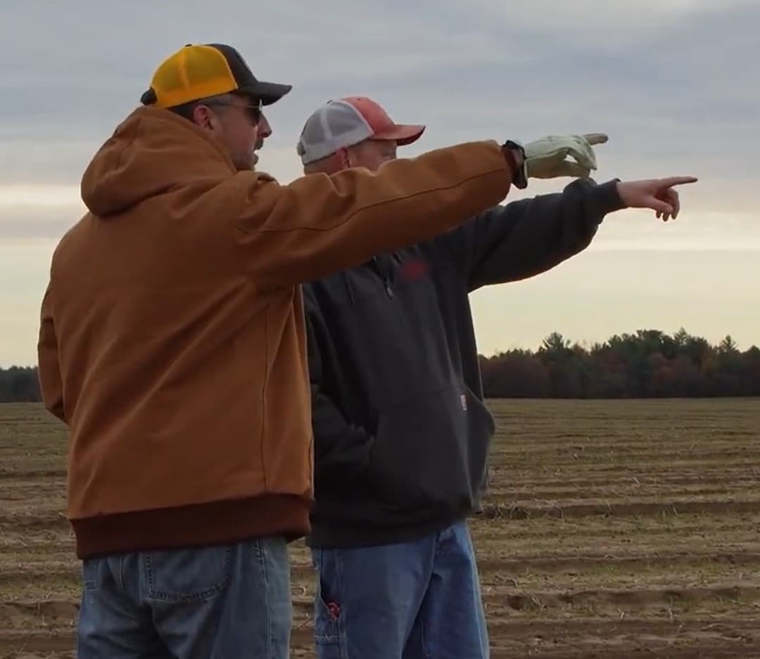 Two farmers point across a tilled field after harvest while planning where to pick rocks