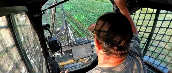 Operator in a tractor cab watches an in-cab display while detection rings highlight spots in the rows ahead
